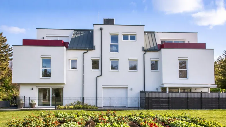 Moderne Reihenhäuser mit weißer Fassade und gepflegtem Gemüsegarten im Vordergrund.