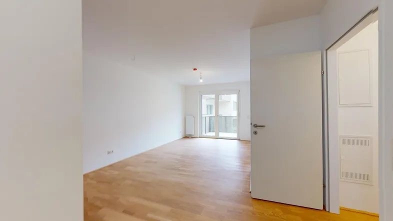 Helles, leeres Zimmer mit Parkettboden und Zugang zu einem Balkon, ideal als Wohnbereich.
