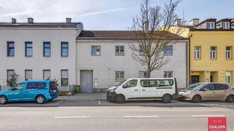 Ansicht der Gebäudefassade von der Straße mit parkenden Autos davor.