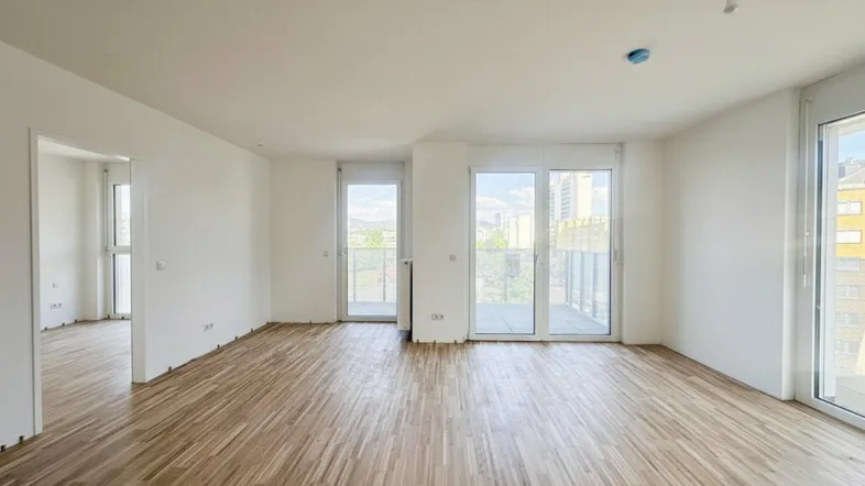 Heller Wohnraum mit Parkettboden und Zugang zu einem Balkon, bereit für die Einrichtung.