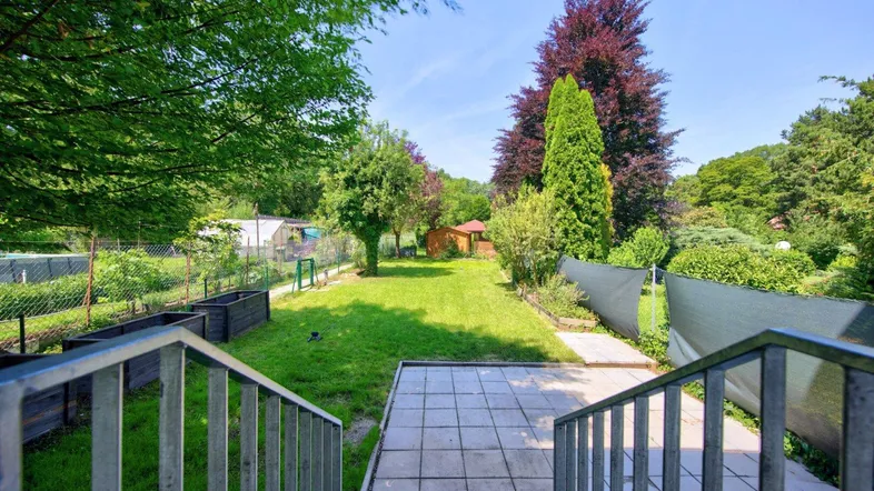 Gepflasterte Terrasse mit Treppe, die zu einem weitläufigen grünen Garten mit Rasenfläche führt.