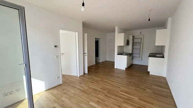 Heller, offener Wohnbereich mit Parkettboden und Zugang zu einem Balkon oder einer Loggia.