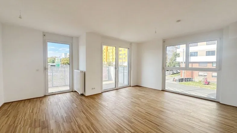 Helles Wohnzimmer mit Parkettboden und großen Fenstern, die viel Tageslicht hereinlassen.