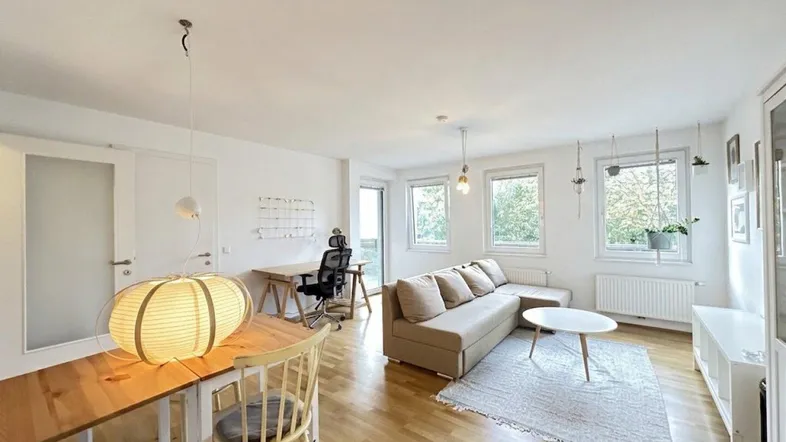 Heller und offener Wohn-Essbereich mit Parkettboden, gemütlichem Sofa und einem funktionalen Arbeitsplatz.