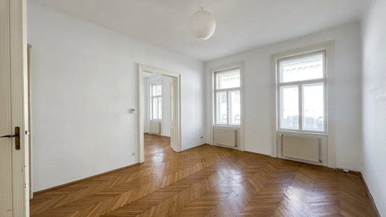 Helles Zimmer mit Fischgrätparkettboden und zwei großen Fenstern, gut gepflegt.