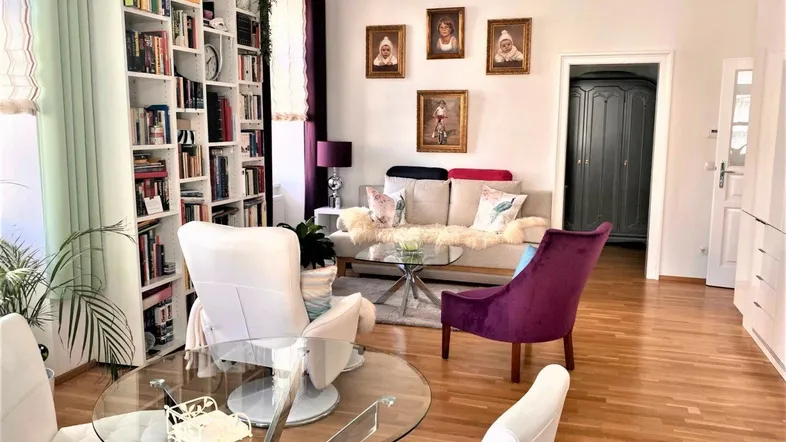 Helles Wohnzimmer mit großem Bücherregal, bequemen Sitzgelegenheiten und Holzboden.