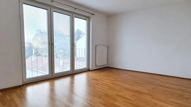 Helles Zimmer mit Parkettboden und großen Fenstern, die Zugang zu einem Balkon bieten.