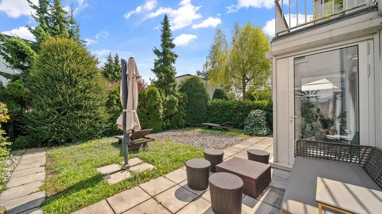 Gepflegter Gartenbereich mit gepflasterter Terrasse, Sitzgelegenheiten und üppiger Bepflanzung.