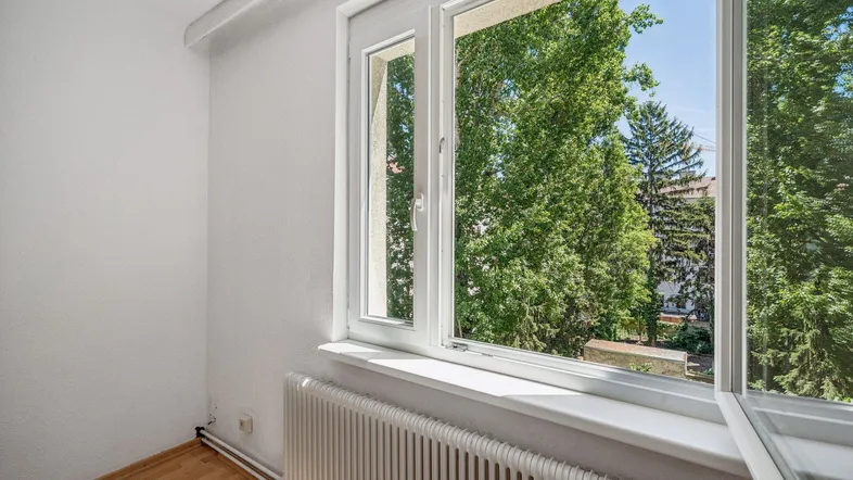 Helles Zimmer mit Parkettboden und großem Fenster mit Blick ins Grüne.