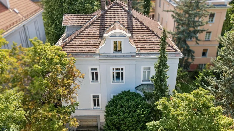 Historische Villa mit klassischer Architektur und gepflegtem Dach in grüner Umgebung.