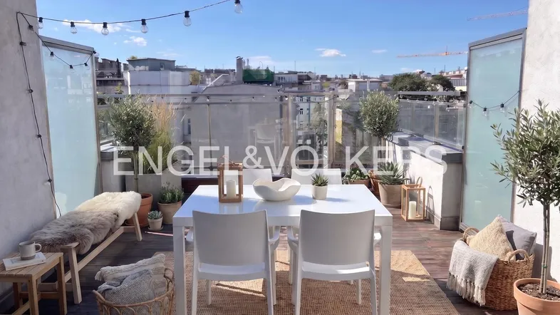 Geräumige Dachterrasse mit Esstisch, Pflanzen und Lichterkette, bietet einen weiten Blick über die Stadt.