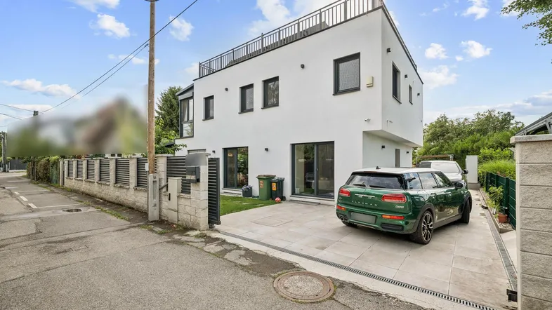 Moderne weiße Villa mit Flachdach, großem Vorplatz und gepflasterter Einfahrt.