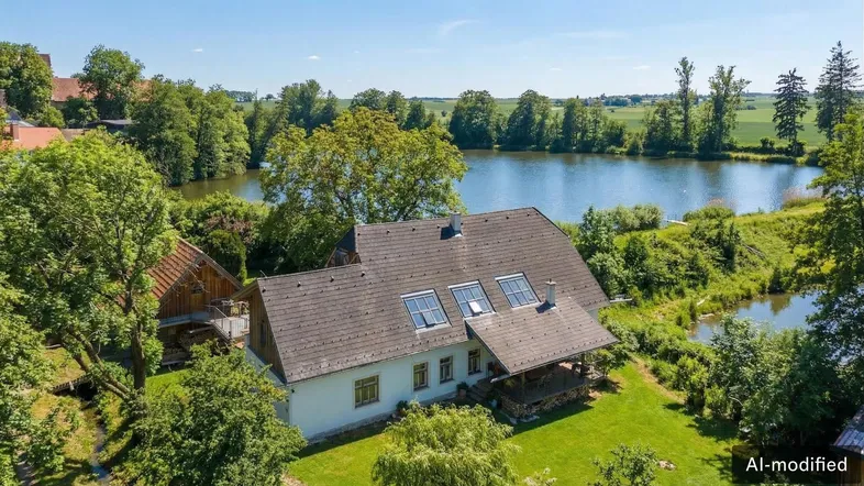 Idyllisches Haus am See mit grüner Umgebung und Bäumen unter blauem Himmel.