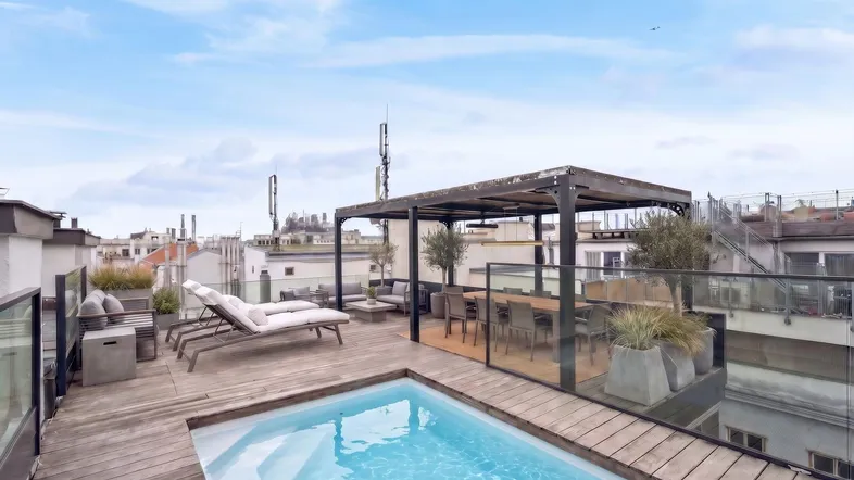 Dachterrasse mit kleinem Pool, Sonnenliegen und Essbereich unter einer Pergola mit Stadtblick.
