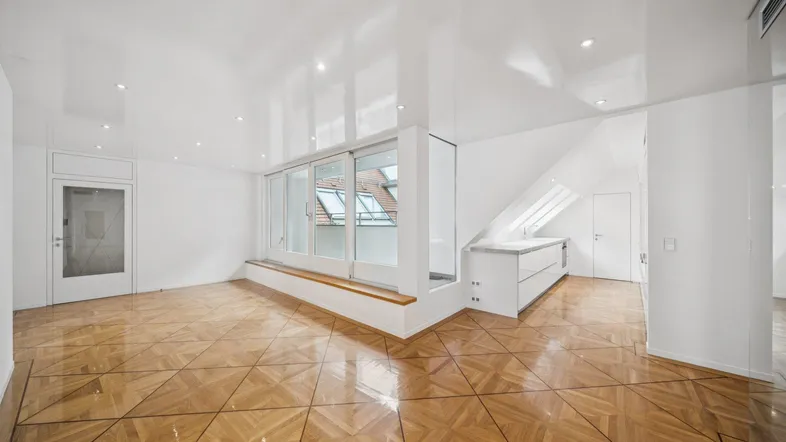 Geräumiger, heller Wohnbereich mit elegantem Parkettboden und großen Fenstern unter einer Dachschräge.