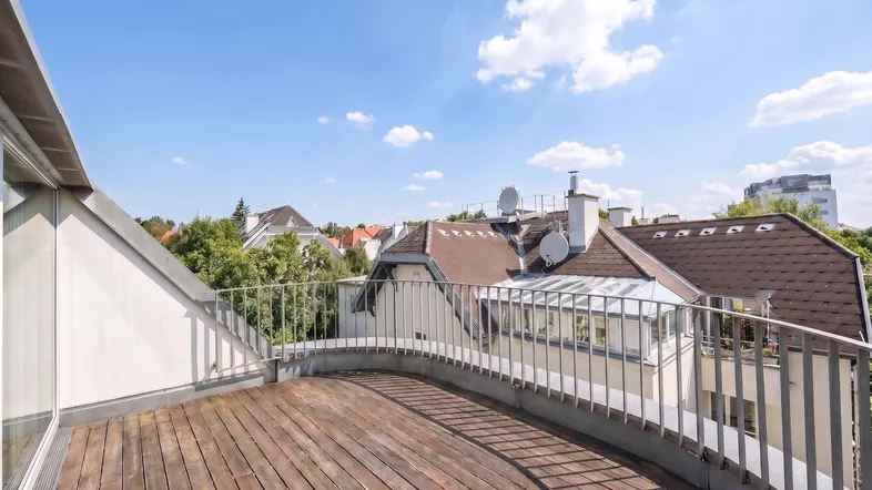 Geräumige Dachterrasse mit Holzboden und Blick über die Dächer der Stadt unter blauem Himmel.