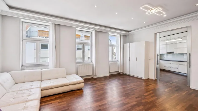 Helles Wohnzimmer mit dunklem Parkettboden, weißer Couch und offenem Zugang zur modernen Küche.