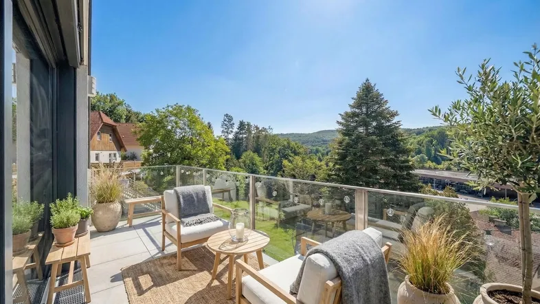 Heller Balkon mit Glasgeländer, bequemen Gartenmöbeln und weitem Blick ins Grüne.