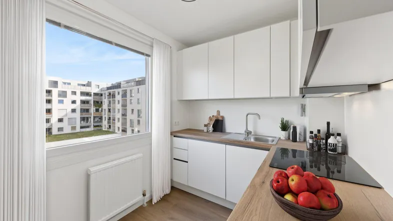 Moderne Küche mit weißen Schränken, Holzarbeitsplatte und Blick auf die umliegenden Gebäude.