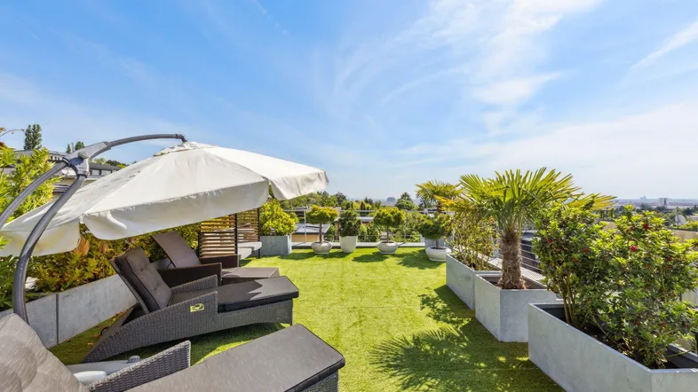 Große Dachterrasse mit Kunstrasen, bequemen Liegestühlen und Pflanzen für entspannte Stunden im Freien.
