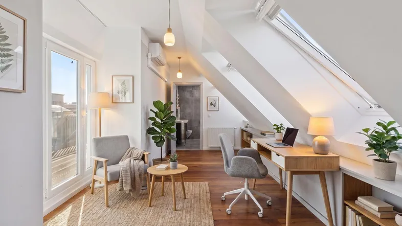 Helles Dachgeschosszimmer mit Holzboden, Schreibtisch und gemütlicher Sitzecke, ideal als Wohn- oder Arbeitsbereich.