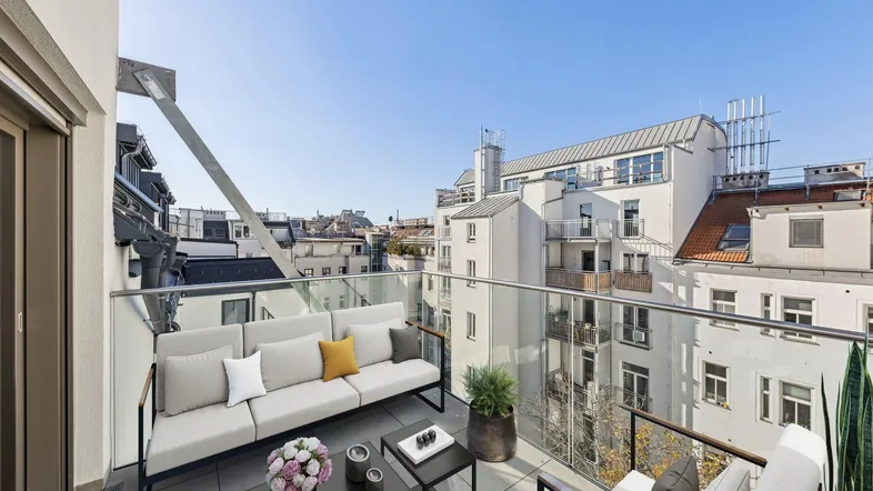 Möblierter Balkon mit Glasgeländer und weitem Blick über die Stadt.