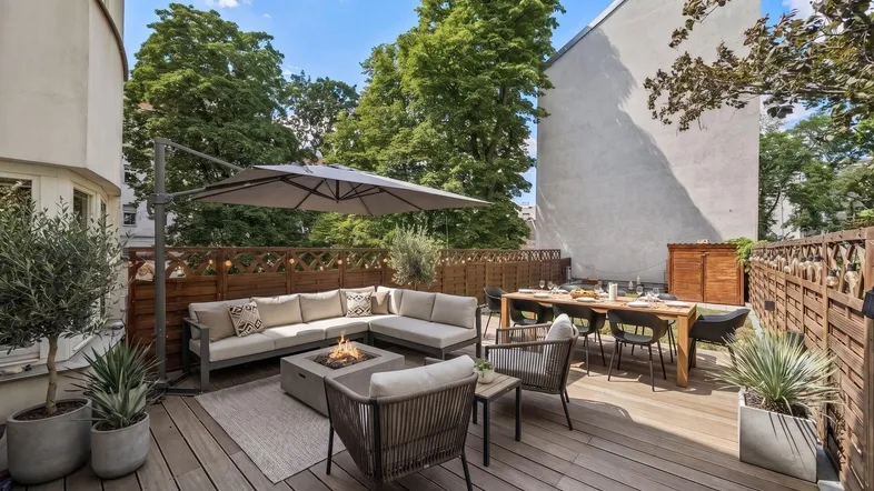 Große möblierte Terrasse mit Holzboden, Sitzgelegenheiten, Esstisch und Feuerstelle unter Sonnenschirm.