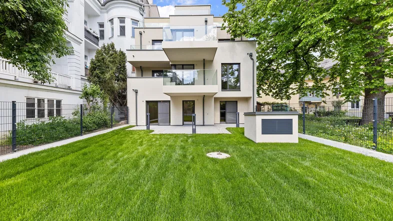 Modernes Gebäude mit gepflegtem Rasen, Terrasse und Balkonen in grüner Umgebung.