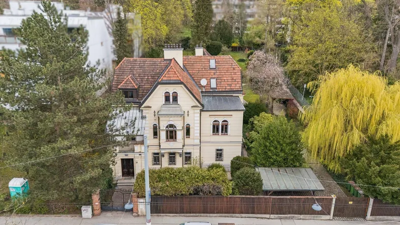 Historische Villa mit klassischer Architektur, umgeben von altem Baumbestand und üppigem Grün.