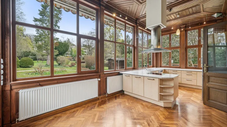 Helle Küche mit Kochinsel, Holzboden und großen Fenstern mit Blick in den Garten.
