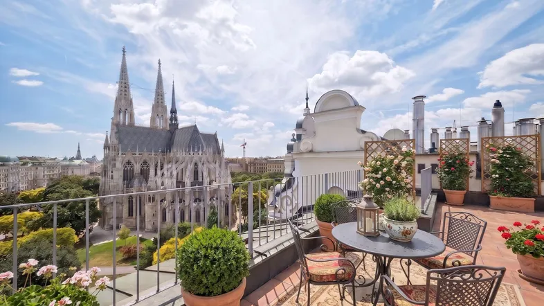 Große Dachterrasse mit Sitzgelegenheiten, Pflanzen und beeindruckendem Blick auf die Votivkirche.