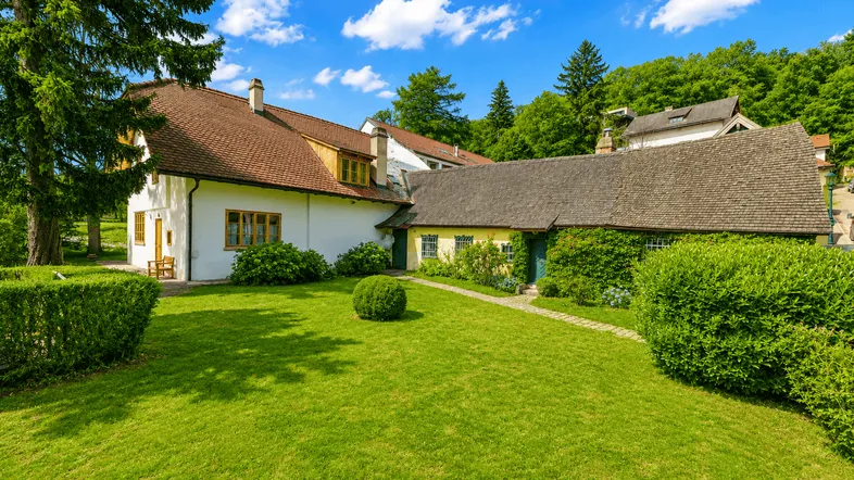 Historisches Gebäude mit gepflegtem Garten und grüner Umgebung unter blauem Himmel.