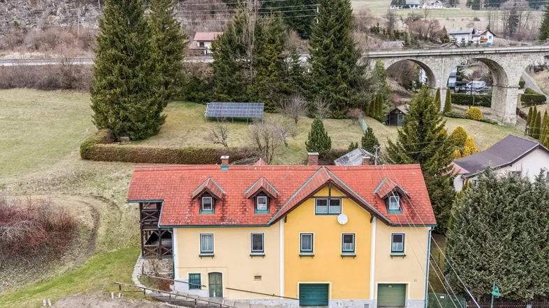 Luftaufnahme eines Hauses mit rotem Ziegeldach, gelber Fassade und grüner Umgebung in ländlicher Lage.