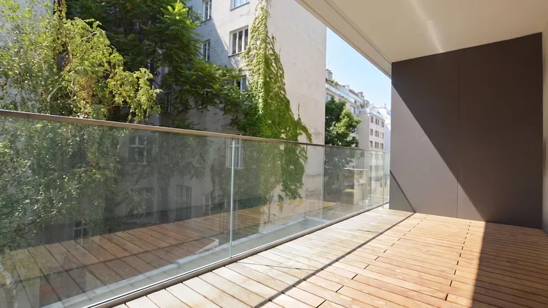 Geräumiger Balkon mit Holzfußboden und Glasgeländer, bietet einen grünen Ausblick auf die Umgebung.