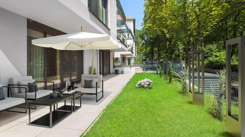 Großzügige Terrasse mit modernen Gartenmöbeln und Sonnenschirm, umgeben von gepflegtem Rasen und Bäumen.