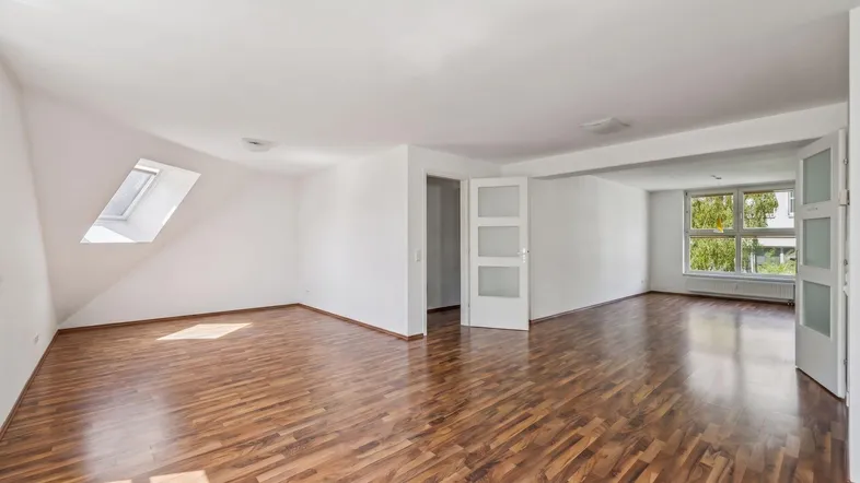 Helles, leeres Zimmer mit Holzboden, Dachfenster und großen Fenstern, bereit zur individuellen Gestaltung.