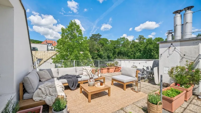 Möblierte Dachterrasse mit bequemen Loungemöbeln, Pflanzen und weitem Blick ins Grüne unter blauem Himmel.