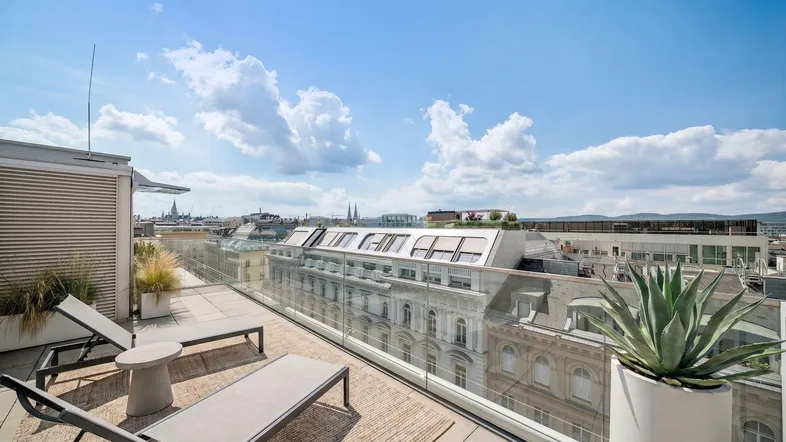 Geräumige Dachterrasse mit Liegestühlen und weitem Blick über die Stadt und umliegende Gebäude.