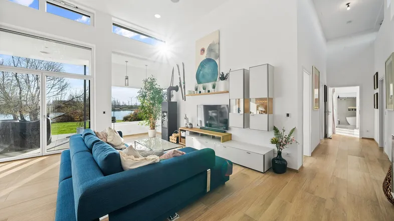Helles, modernes Wohnzimmer mit hohen Decken, Holzboden und direktem Blick auf das Wasser.