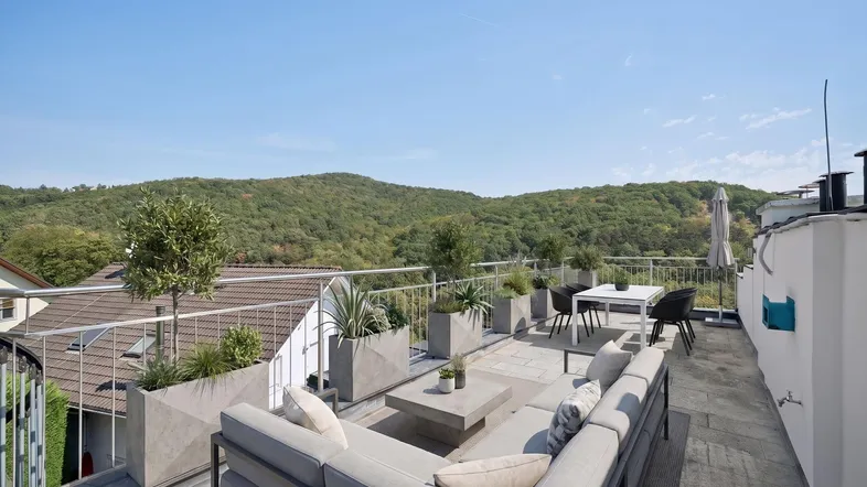 Große Dachterrasse mit modernen Lounge-Möbeln und weitem Blick auf die bewaldeten Hügel.