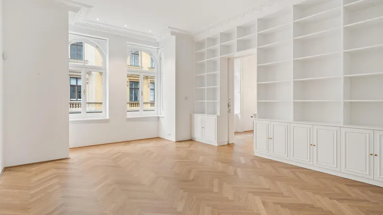 Helles Wohnzimmer mit Fischgrätparkett, hohen Decken und eleganten Einbauregalen.