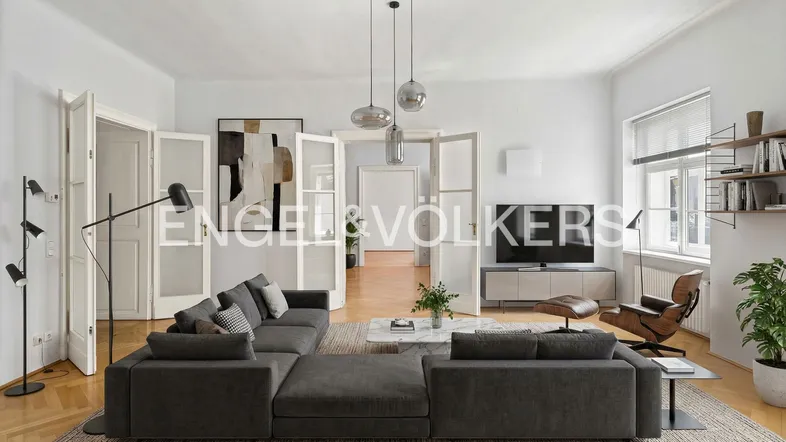 Modernes Wohnzimmer mit großem Ecksofa, Parkettboden und hohen Decken.