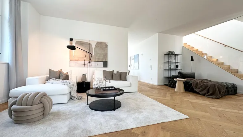 Helles, modernes Wohnzimmer mit Fischgrätparkett, bequemen Sofas und offener Treppe.
