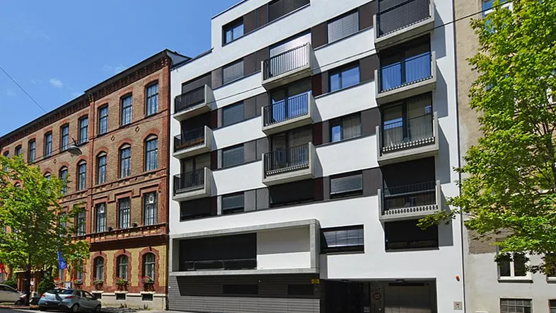 Moderne Fassade eines Neubaus mit Balkonen und Jalousien in städtischer Umgebung.
