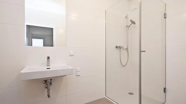 Modernes Badezimmer mit weiß gefliesten Wänden, einem Waschbecken und einer geräumigen Glasdusche.