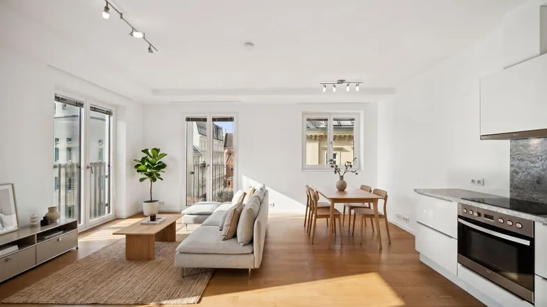 Helles, offenes Wohnzimmer mit integrierter Küche, Essbereich und Zugang zu einem französischen Balkon.