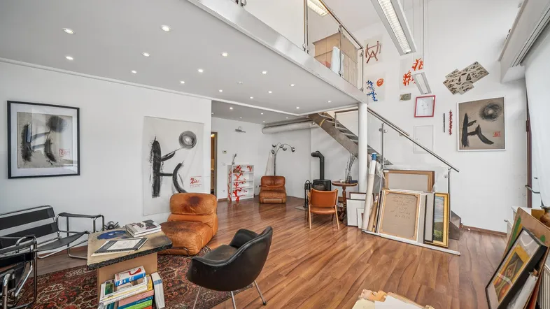 Geräumiges Wohnzimmer mit Holzofen, hohen Decken und Zugang zu einer Galerieebene.
