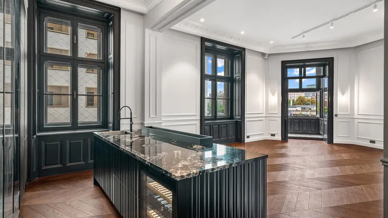 Moderne offene Küche mit dunkler Marmorinsel, Fischgrätparkett und Zugang zum Balkon.