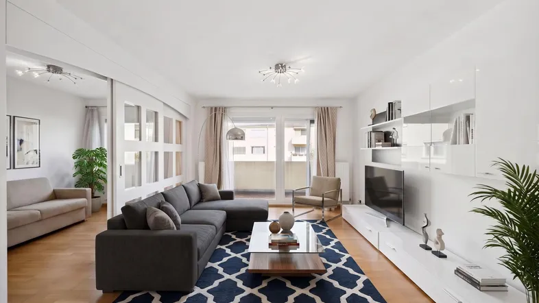 Helles Wohnzimmer mit modernem Sofa, TV-Möbel und Zugang zu einem Balkon.