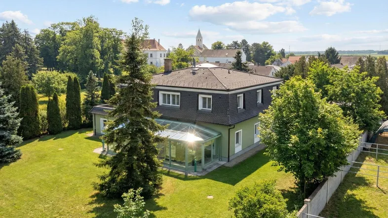 Großzügiges Anwesen mit Wintergarten und weitläufigem Garten, umgeben von Bäumen und ländlicher Idylle.
